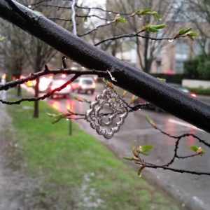 A little silver trinket hanging from a branch with traffic in the background