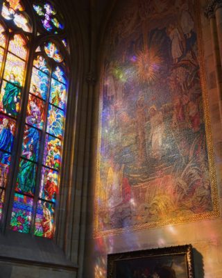 Stained glass throwing rainbow light on a painting of Christ being baptised