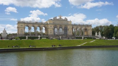 The Gloriette, a large colonnated arcade overlooking a pond, under a mostly blue sky