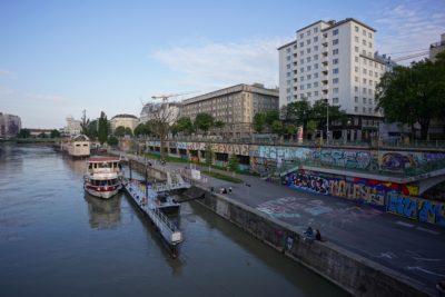 A canal near downtown. There are towers, and boats in the water, and tons of graffiti on the pier