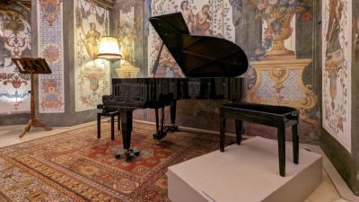 A piano and a couple benches in a small salon with cool Baroque painted walls