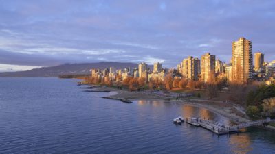 Sunset Beach and West End towers at sunset. The towers are bright gold, reflected in the water, the beach is already in shadow. The sky a bit cloudy and blue