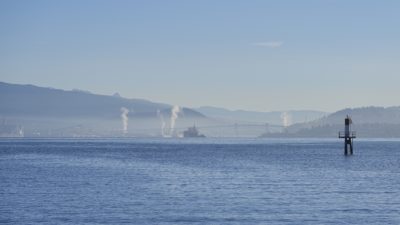 View of the harbour from the Stanley Park Seawall. Everything is blue and a little misty. Second Narrows Bridge is in the distance