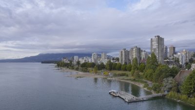 Sunset Beach and West End towers, late afternoon. The trees are green, the towers are silver. The sky is mostly overcast.