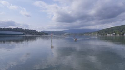 A view of the water from Rocky Point Park, with low mountains in the background. There are some clouds in the sky, reflected in the still water