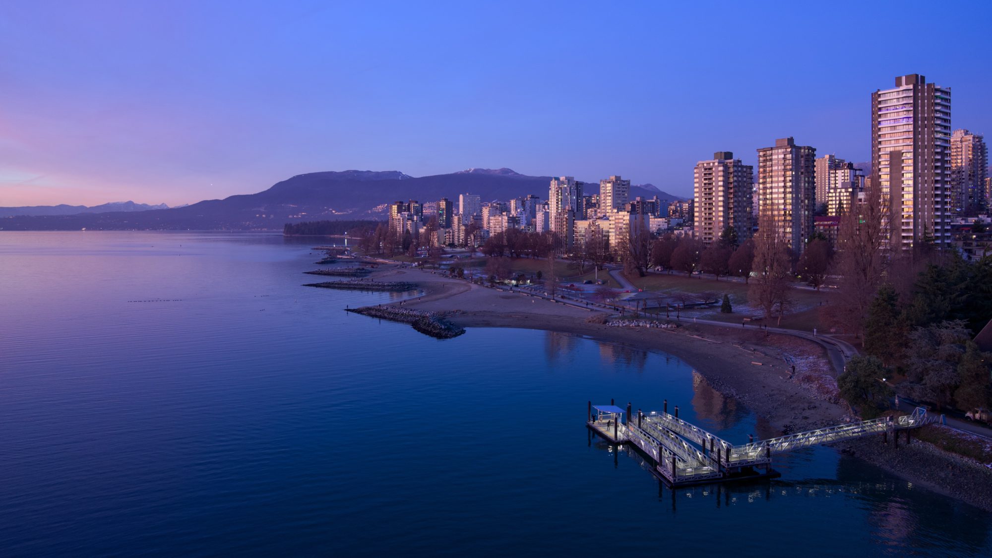 A view of the West End and Sunset Beach from Burrard Bridge. The sky is deep blue with a bit of pink on one end