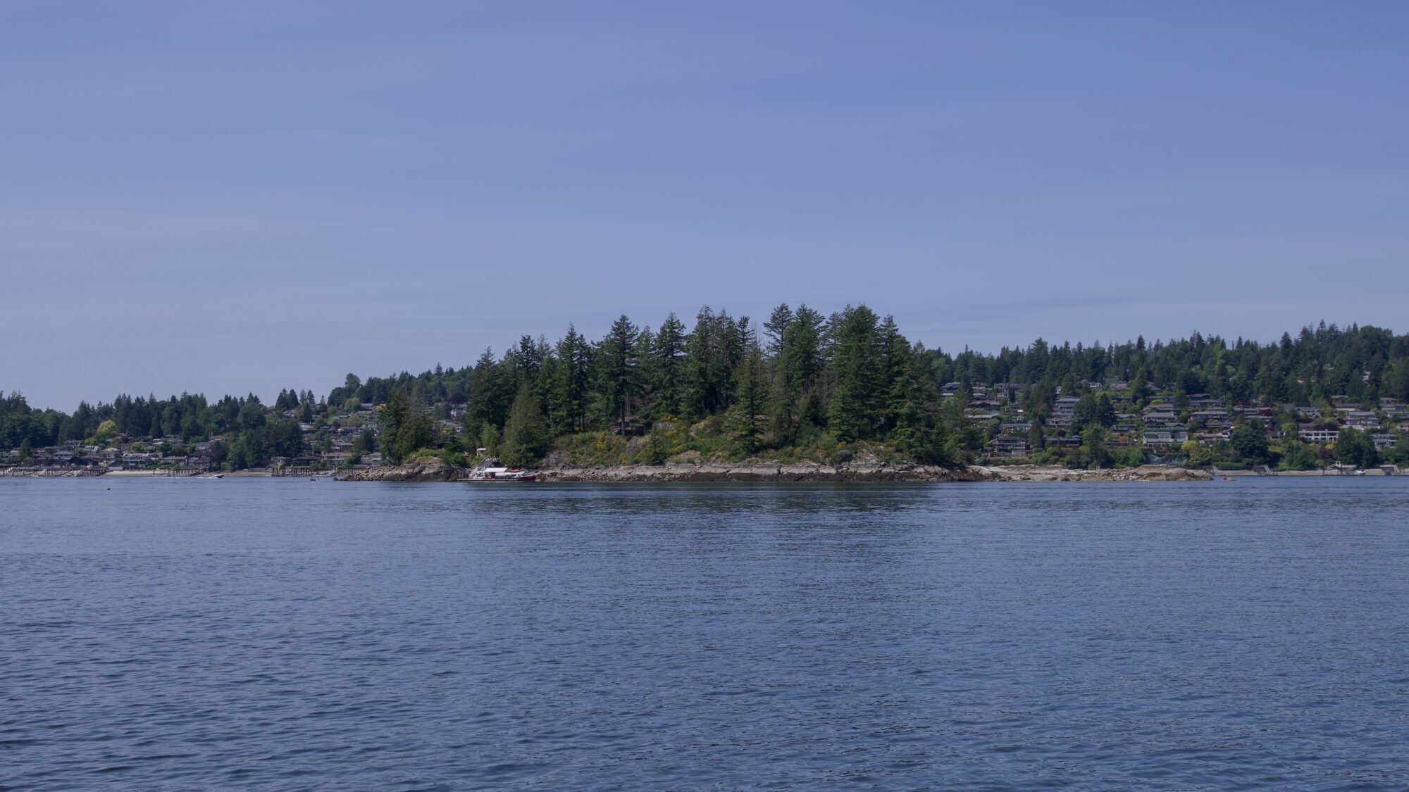 A view from Belcarra Regional Park: Boulder Island and Deep Cove behind it. The sky is solid blue