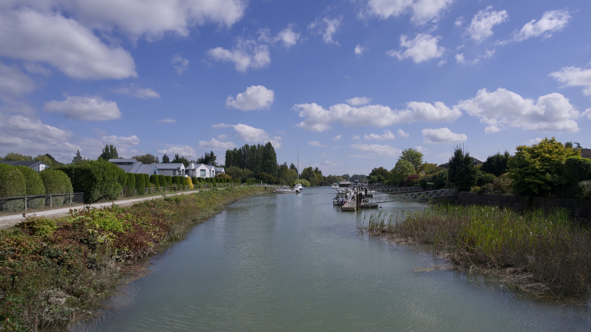 A little canal with some nice houses on one side, under a blue sky with fluffy clouds