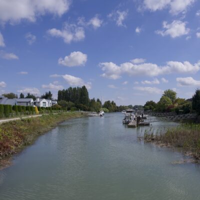 A little canal with some nice houses on one side, under a blue sky with fluffy clouds