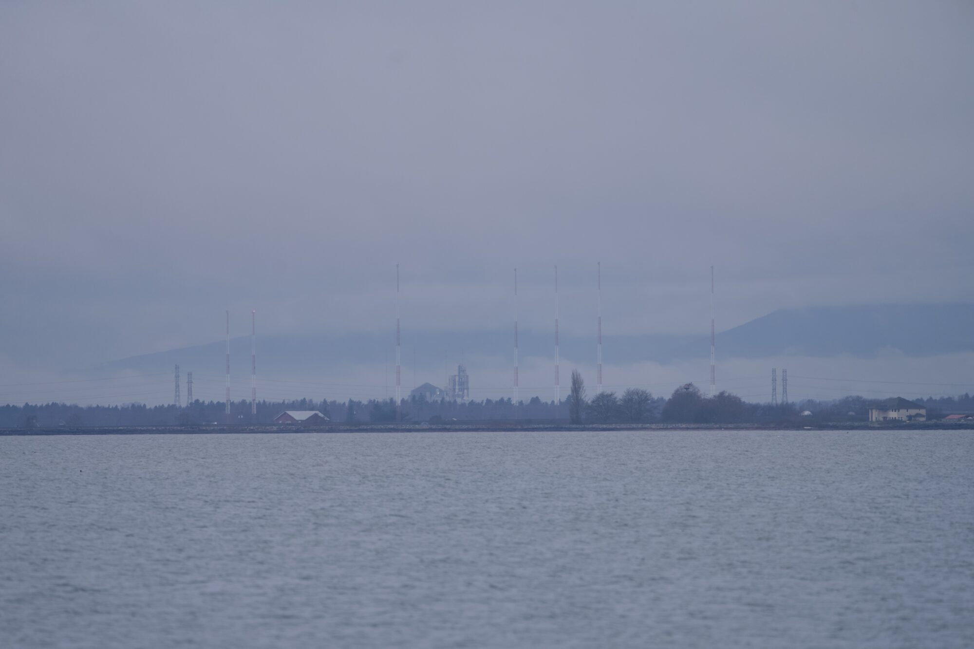 A very grey shot of a faraway shore with some industrial(?) towers