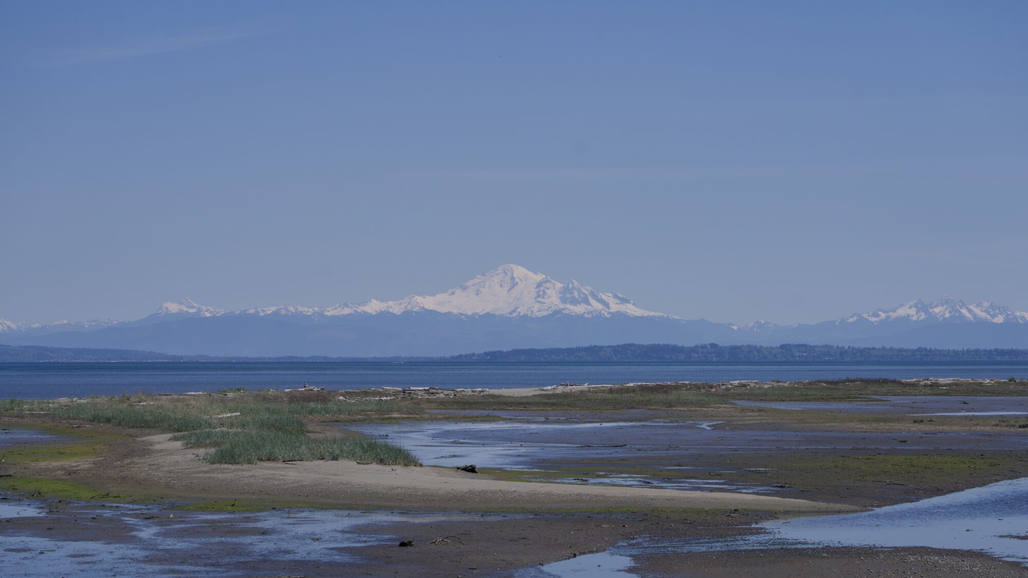 Mount Baker in the distance, over Boundary Bay. In the foreground is low tidal flats, plus a higher and rockier stretch of land